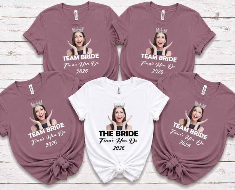 May include: Four mauve t-shirts and one white t-shirt featuring a custom photo print of a person wearing a crown, with the text TEAM BRIDE or THE BRIDE, Tina's Hen Do, and 2026 printed below the image on each garment.