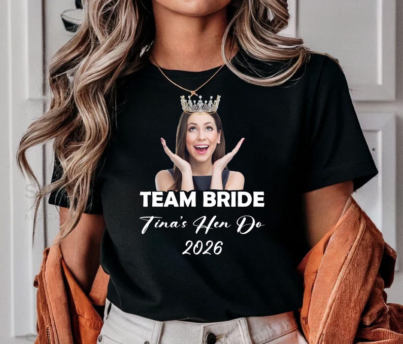 May include: A black short-sleeved t-shirt featuring a graphic of a person wearing a crown, with the text "TEAM BRIDE", "Tina's Hen Do", and "2026" printed in white below the image. The shirt has a crew neckline and a standard fit design.