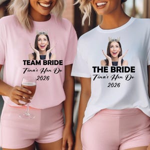 May include: A light pink t-shirt with the text TEAM BRIDE Tina's Hen Do 2026 and a white t-shirt with the text THE BRIDE Tina's Hen Do 2026. Both shirts feature a graphic of a person wearing a crown with hands raised near their face.