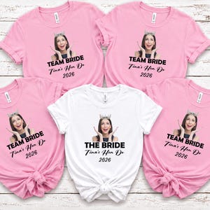 May include: Four light pink t-shirts and one white t-shirt, each featuring a printed photograph of a person wearing a crown, with the text TEAM BRIDE or THE BRIDE, followed by Tina's Hen Do 2026 in black lettering on the front of each garment.