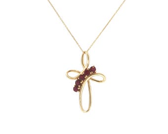 May include: A gold necklace featuring a stylized cross pendant with fluid, looping lines. The center of the cross is accented with a vertical row of five small, round, deep red rubies set into the polished gold metal frame.