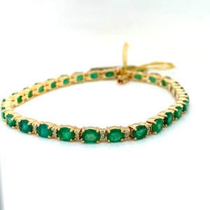 May include: A gold tennis bracelet with oval-shaped emeralds and small diamonds set in the metal.