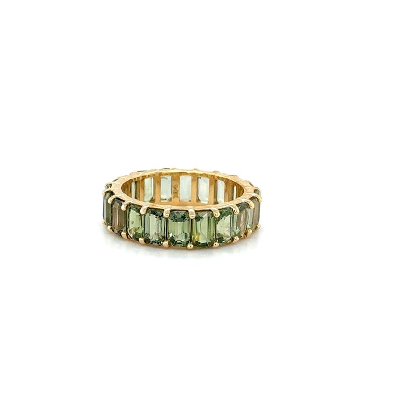 May include: A gold ring with a band of rectangular, olive-green gemstones. The ring is set against a white background, highlighting the ring's design and color.