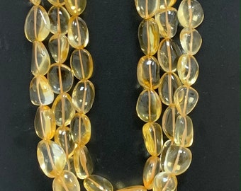 May include: A strand of yellow citrine gemstone beads, each bead is oval shaped and smooth. The beads are strung on a clear thread and are arranged in a loose, flowing pattern.