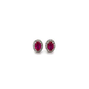 Peut inclure: Une paire de boucles d'oreilles à clous avec des rubis rouge vif taille ovale sertis dans un métal argenté. Chaque rubis central est entouré d'un halo de petites pierres blanches rondes et transparentes, créant un design classique et symétrique.