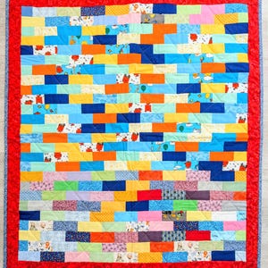 May include: A vibrant patchwork quilt with a red border. The quilt features rectangular fabric pieces in shades of blue, orange, yellow, and green. Some pieces have cartoon character prints. The quilt is a handmade item, suitable for a bed or a sofa.