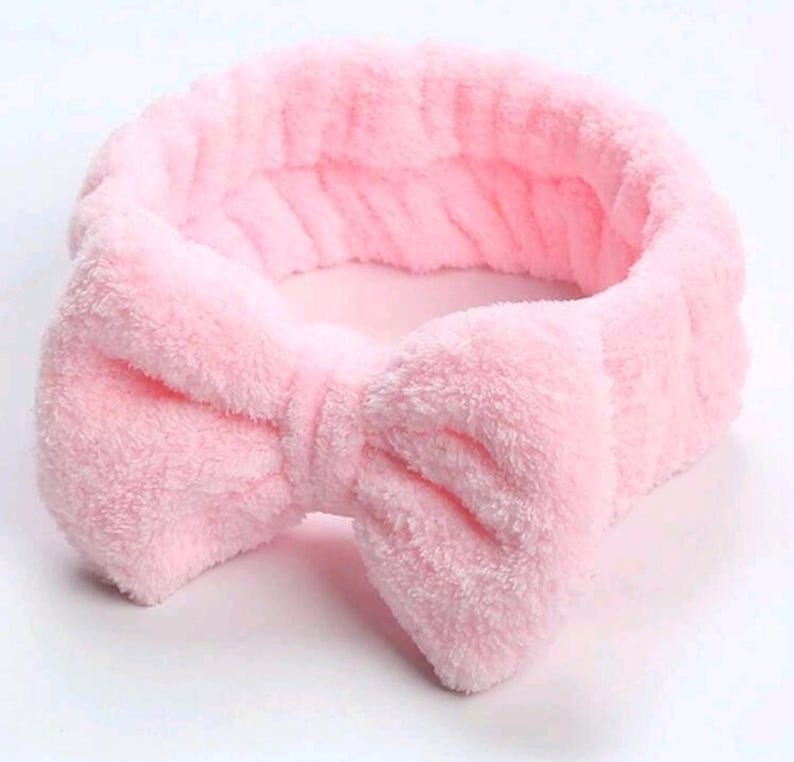 Op de afbeelding: Een zachte, lichtroze spa-haarband met een grote strik in het midden. De haarband is gemaakt van een zacht, pluche materiaal, perfect om haar uit het gezicht te houden tijdens huidverzorging of make-up. De strik voegt een vleugje charme toe.