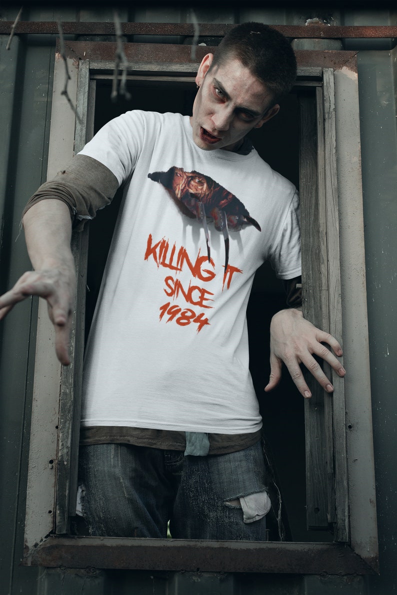 K&ouml;nnte beinhalten: Ein wei&szlig;es T-Shirt mit einer roten Grafik eines gruseligen Gesichts und dem Text "Killing It Since 1984".