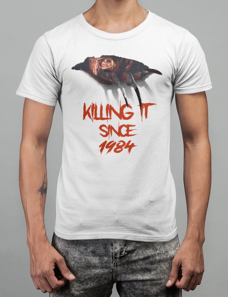 K&ouml;nnte beinhalten: Wei&szlig;es T-Shirt mit einer roten Grafik von Freddy Krueger's Hand und Gesicht mit dem Text "Killing It Since 1984".