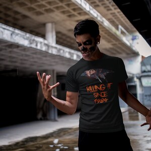K&ouml;nnte beinhalten: Ein schwarzes T-Shirt mit einem Aufdruck eines Charakters aus dem Film "Freitag der 13." mit einem Messer. Der Text "Killing it since 1984" ist auf dem Shirt gedruckt.