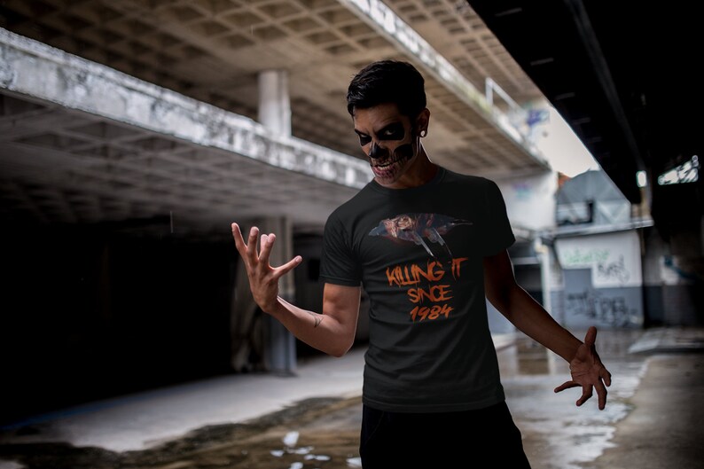 K&ouml;nnte beinhalten: Ein schwarzes T-Shirt mit einem Aufdruck eines Charakters aus dem Film "Freitag der 13." mit einem Messer. Der Text "Killing it since 1984" ist auf dem Shirt gedruckt.