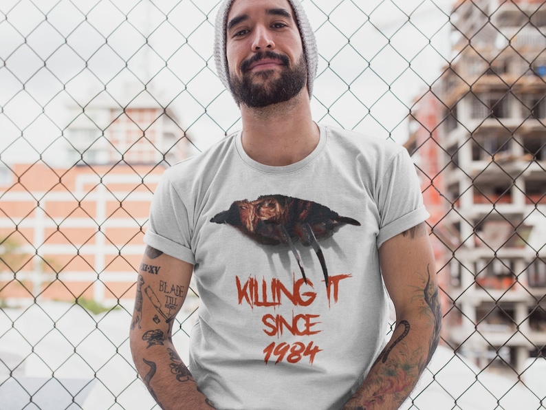 K&ouml;nnte beinhalten: Ein wei&szlig;es T-Shirt mit einem Aufdruck von Freddy Kruegers Handschuh und dem Text "Killing It Since 1984".
