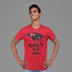 K&ouml;nnte beinhalten: Ein rotes T-Shirt mit einem Aufdruck eines Charakters aus dem Film Freitag der 13.. Der Text "Killing It Since 1984" ist unter dem Aufdruck gedruckt.