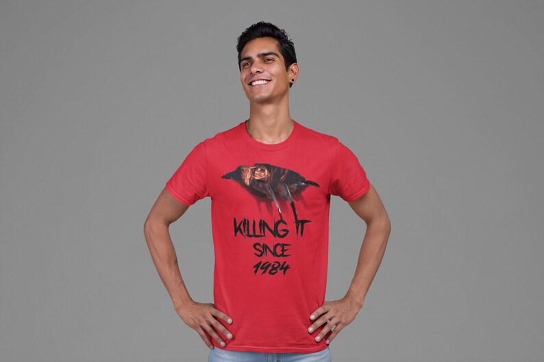 K&ouml;nnte beinhalten: Ein rotes T-Shirt mit einem Aufdruck eines Charakters aus dem Film Freitag der 13.. Der Text "Killing It Since 1984" ist unter dem Aufdruck gedruckt.