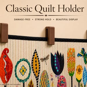 May include: Three brown, rectangular, ribbed quilt holders mounted on a wall, securing a quilted fabric panel. The text "Classic Quilt Holder" appears above, with the subtext "DAMAGE-FREE • STRONG HOLD • BEAUTIFUL DISPLAY" below it.
