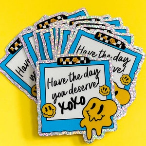 Könnte beinhalten: Ein Stapel blauer und silberner holografischer Aufkleber mit einem Smiley und dem Text "Have the day you deserve! xoxo".