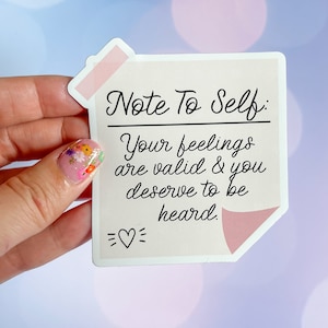 May include: A sticker with the text "Note To Self: Your feelings are valid & you deserve to be heard." The sticker is light pink with a pink tape detail and a heart symbol.