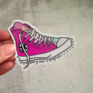 May include: Pink glitter Converse-style sneaker with white laces and a black star. The sticker has the text "every step is progress".