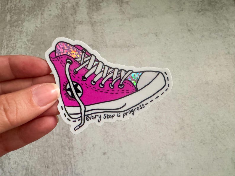 May include: Pink glitter Converse-style sneaker with white laces and a black star. The sticker has the text "every step is progress".