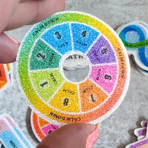 Puede incluir: Un spinner circular de colores con las palabras "Calm Down" repetidas alrededor del borde. El spinner está dividido en ocho secciones, cada una con un color diferente y un número del 1 al 8. El centro del spinner es un círculo blanco con la palabra "MATH" escrita en negro.