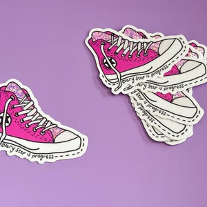 May include: Pink glitter high top sneakers with white laces and a black star on the side. The sneakers are on a sticker with the text "Every step is progress" repeated multiple times.