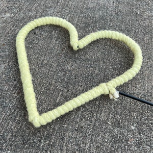 May include: A light green yarn heart-shaped object with a black stick attached to it.
