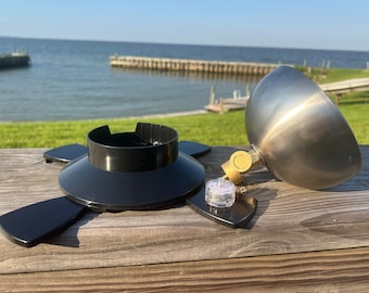 May include: A disassembled outdoor solar light with a black base, a silver dome, and a clear glass lens. The light is sitting on a wooden surface.