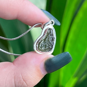 May include: A silver heart-shaped pendant with a green aventurine stone. The pendant is on a silver chain.