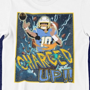 May include: White t-shirt featuring a graphic of a football player in a blue and yellow uniform, throwing a football. The design includes lightning bolts and the words "CHARGED UP!!" in yellow and blue.