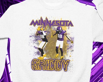 May include: White sweatshirt featuring a graphic of two football players in purple and gold uniforms. The word "MINNESOTA" is arched above the players, and "GRIDDY" is printed below. The design has a distressed, vintage look.