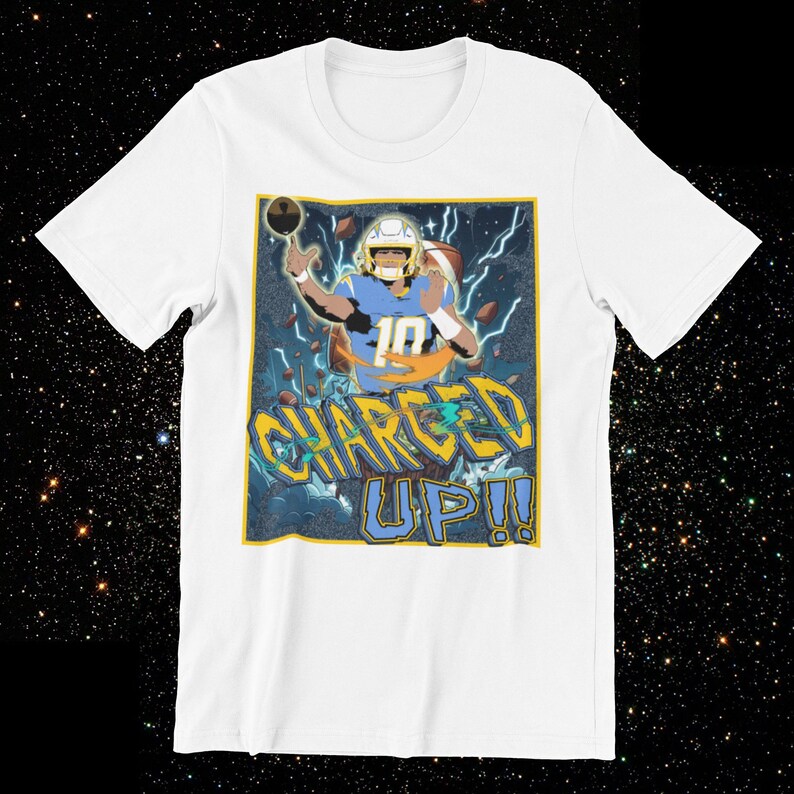 May include: White t-shirt featuring a graphic of a football player in a blue and yellow uniform throwing a football. The text "CHARGED UP!!" is displayed in a stylized font below the player.