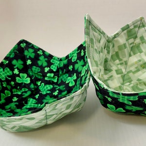 Peut inclure: Deux bols en tissu vert avec un motif trèfle. Les bols sont pliés et ont un motif à carreaux blanc et vert à l'intérieur.