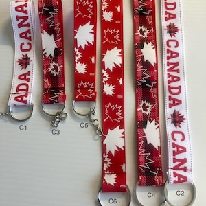 May include: Six red, white and black keychains with different designs featuring maple leaves and the word "CANADA". The keychains are labelled C1, C2, C3, C4, C5 and C6.