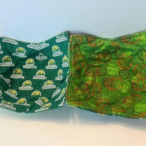 May include: Two fabric bowl covers. One is green with Seattle SuperSonics logos in yellow and white. The other is green with orange and black basketball designs. Both are open at the top and folded at the sides.