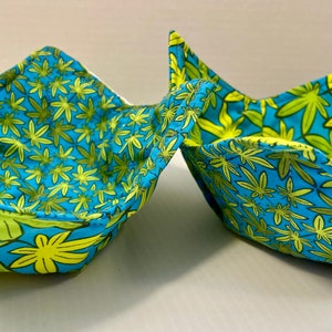 May include: Two blue and green fabric bowls with a leaf pattern. The bowls are folded and ready to be used.