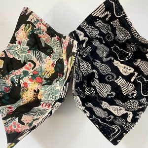May include: Two fabric bowls with black cat designs. One bowl has a black and white cat pattern on a black background. The other bowl has a black cat pattern on a cream background with green and red floral accents.