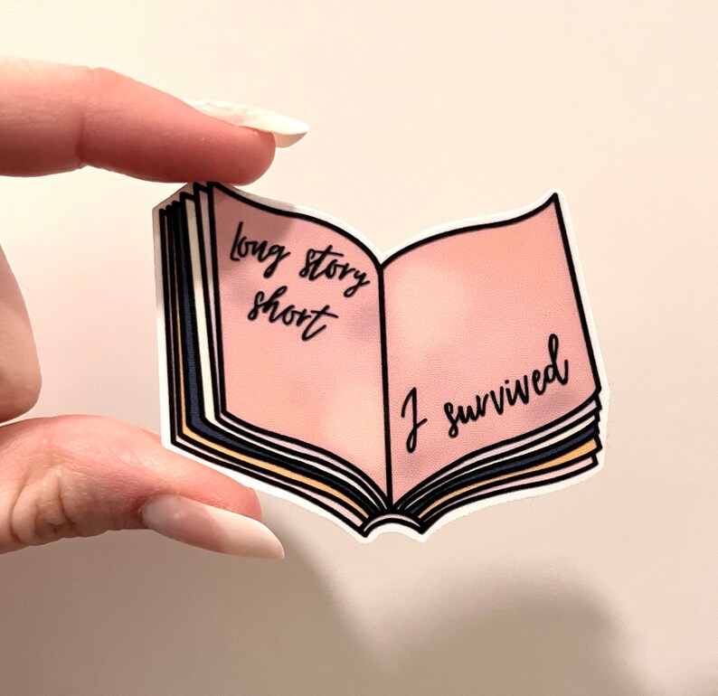 May include: A sticker in the shape of an open book with the words "long story short" and "I survived" in black script. The book's pages are pink, with a white border and black, yellow, and blue details.