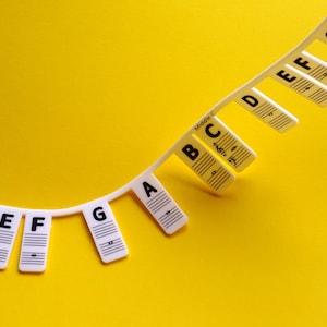 May include: White plastic music note chart with the letters A through G printed on each note. The chart is curved and the notes are hanging down. The text "Middle C" is printed on the chart.