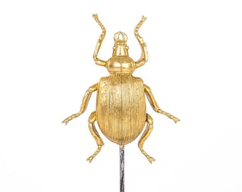 Peut inclure: Une figurine de scarabée dorée sur un support en métal noir avec une base ronde. Le scarabée a un corps détaillé et texturé et de longues pattes.