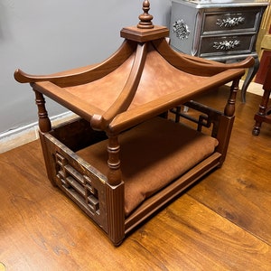 May include: A wooden dog bed with a pagoda-style roof. The bed has a brown cushion and a decorative lattice design on the sides.