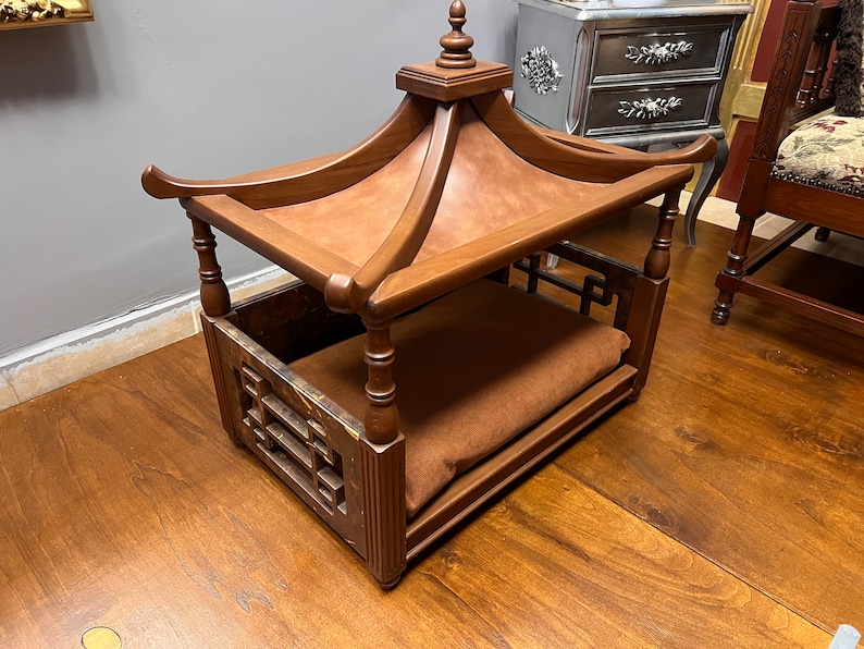 May include: A wooden dog bed with a pagoda-style roof. The bed has a brown cushion and a decorative lattice design on the sides.