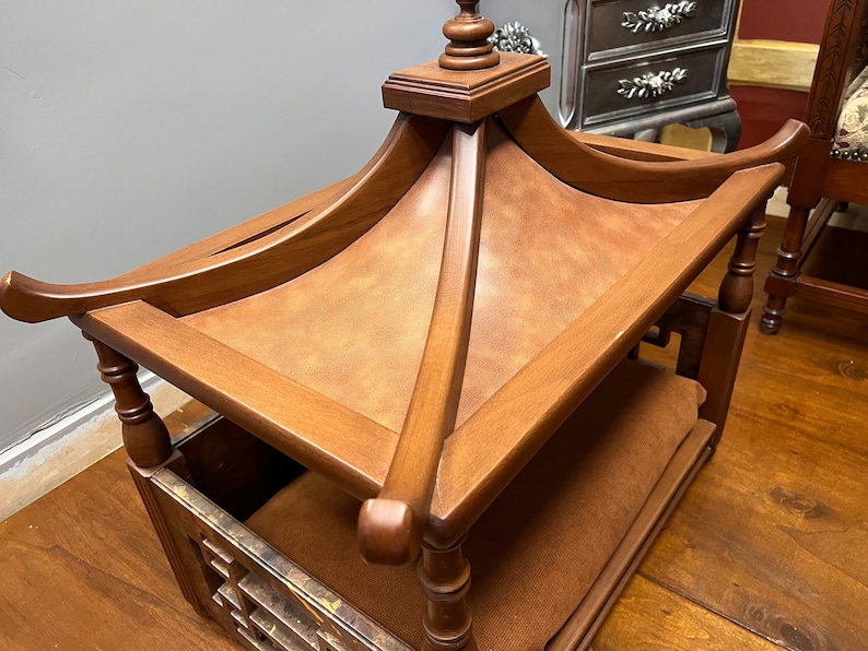 May include: A wooden dog bed with a pagoda-style roof. The bed is made of dark brown wood and has a brown fabric lining. The roof is topped with a finial.
