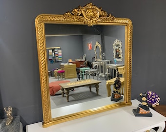 May include: A large, ornate gold-framed mirror with a decorative design. The mirror is reflecting a room with furniture and other decorative items.