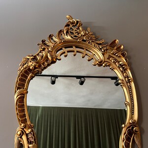 May include: A gold ornate mirror with a decorative, intricate frame. The mirror is oval shaped and has a beveled edge.