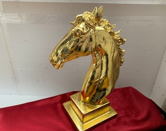 May include: A gold-colored horse head sculpture on a square base. The sculpture is made of a smooth, shiny material and has a realistic design.