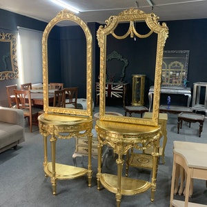 Könnte beinhalten: Zwei vergoldete, verzierte Konsolentische mit Spiegeln. Jeder Tisch hat eine geschwungene Ablage und eine obere Ablage. Die Spiegel haben verzierte Rahmen mit einer goldenen Oberfläche.