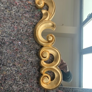 May include: A gold-colored decorative mirror frame with ornate scrollwork. The frame is made of a lightweight material and has a smooth, polished finish.