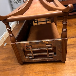 May include: A wooden dog bed with a pagoda-style roof. The bed has a brown cushion and intricate carvings on the sides.