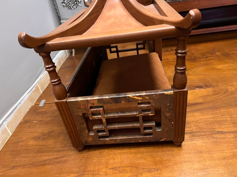 May include: A wooden dog bed with a pagoda-style roof. The bed has a brown cushion and intricate carvings on the sides.