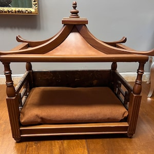 May include: A wooden dog bed with a pagoda-style roof. The bed has a brown cushion and is made of dark wood.